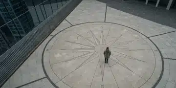 An aerial view of a person standing on a large concrete compass rose in a city plaza, surrounded by modern buildings, symbolizing financial navigation and strategic investment decisions.