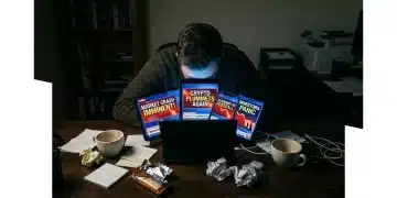A person hunched over a desk, illuminated by multiple glowing screens displaying sensational finance news headlines, symbolizing information overload and poor investment decisions.